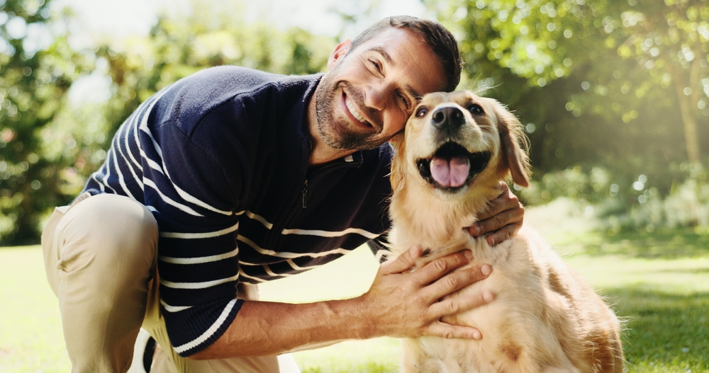 Smiling man kneeling outdoors with his golden retriever