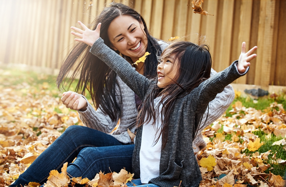 Mother and daughter laughing as they play in autumn leaves