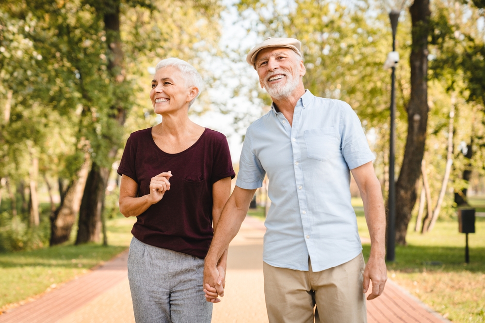 Smiling senior couple walking hand in hand along a park path