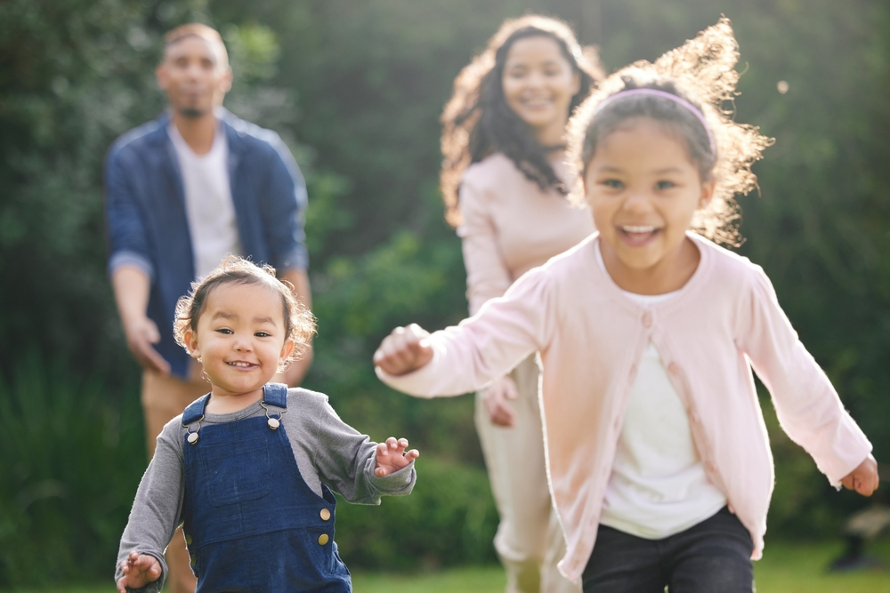 Smiling family running toward the camera across a sunny lawn